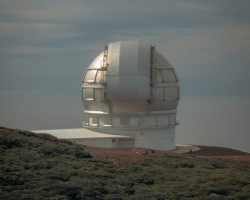 A vertical shot of an observatory building on a mountain near a grassy field