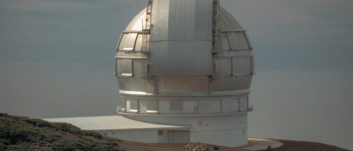 A vertical shot of an observatory building on a mountain near a grassy field